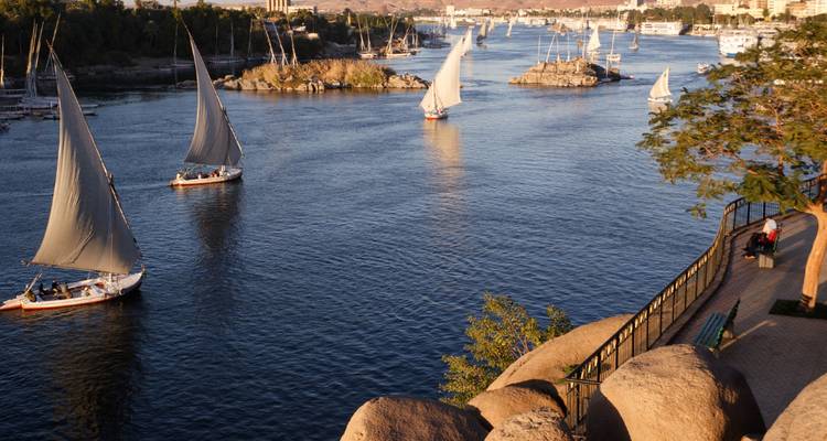 Les felouques traditionnelles aux voiles blanches glissant le long du Nil près des îlots rocheux au coucher du soleil
