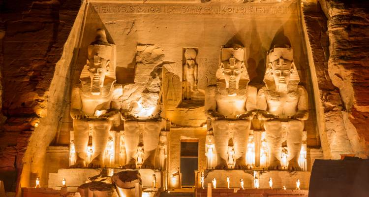 Les statues colossales illuminées gardent l'entrée du temple d'Abu Simbel, taillées dans une falaise de grès et brillant chaleureusement contre le ciel nocturne sombre.