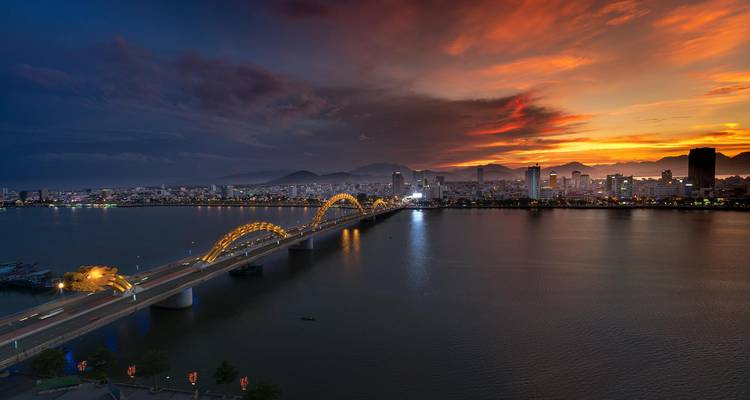 Pont doré enjambant un grand fleuve avec horizon urbain au crépuscule.