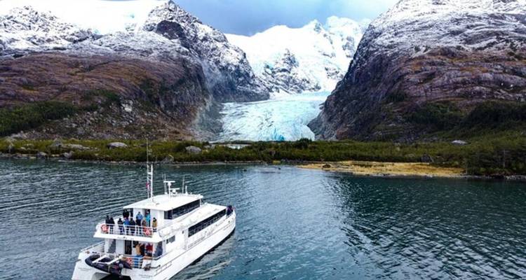 Bote de excursión navegando hacia un glaciar azul ubicado entre los picos patagónicos más escarpados.