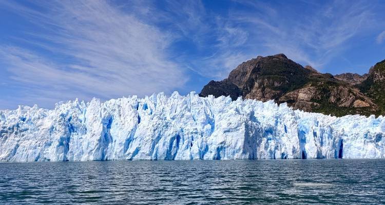 Enorme pared de hielo del glaciar San Rafael que se eleva desde aguas turquesas con montañas al fondo
