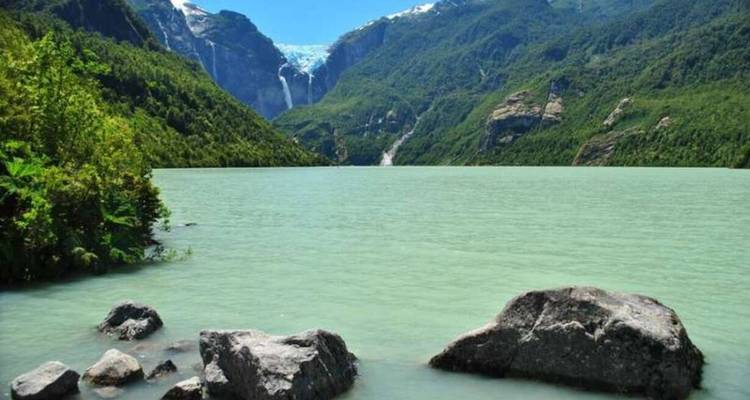 Lago turquesa enmarcado por laderas boscosas y una cascada de glaciar colgante a lo lejos