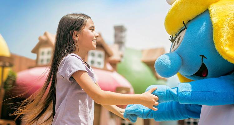 Glimlachend jong meisje dat handjes vasthoudt met een verkleed blauw tekenfilmkarakter in een themapark.