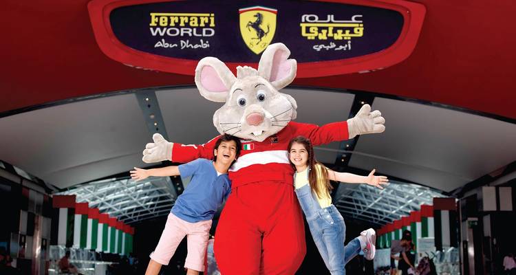 Ferrari World mascotmuisje poseert met twee blije kinderen in de ingangtunnel van het attractiepark.