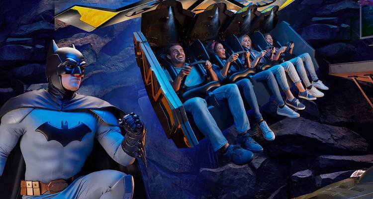 Enthousiaste reizigers zwevend aan een Batman-thema indoor achtbaan naast een levensgrote superheldenfiguur.