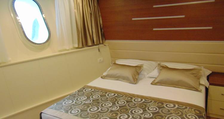 Interior de una cabina con una cama individual y un ojo de buey.