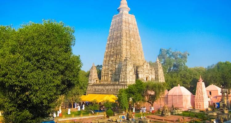 Een grote stenen tempel met een hoge piramidevormige spits, omgeven door bomen en een blauwe lucht.