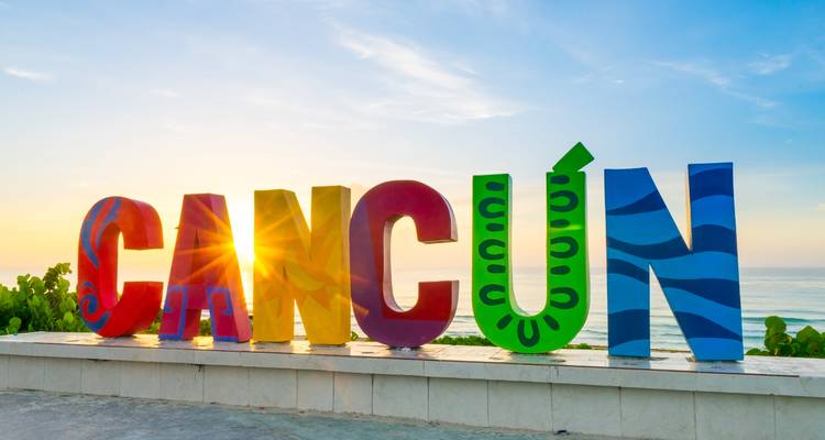 Panneau coloré "Cancun" avec l'océan en arrière-plan au coucher du soleil.