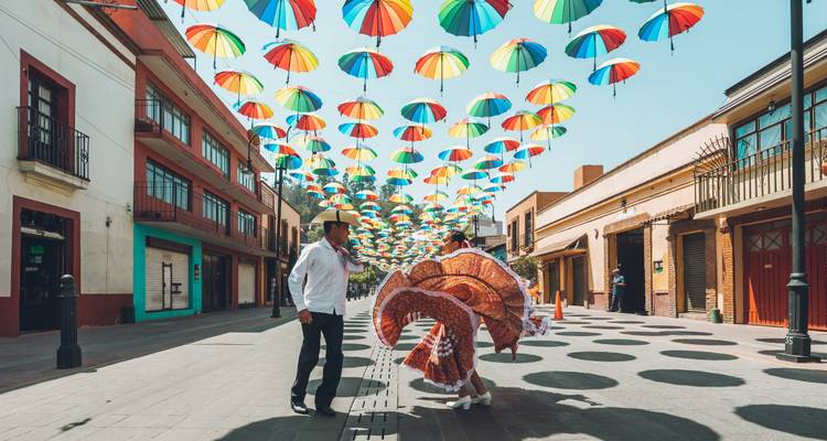A couple dancing on a street decorated with colorful umbrellas.