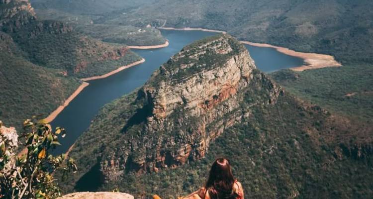 Persoon zittend op een richel met uitzicht op een canyon met een kronkelende rivier.