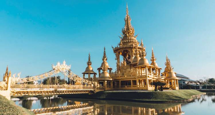 A golden temple with ornate details reflected in a surrounding pond.