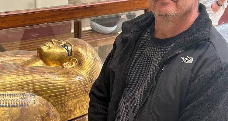 Homme posant à côté d'un sarcophage doré à l'intérieur d'un musée.