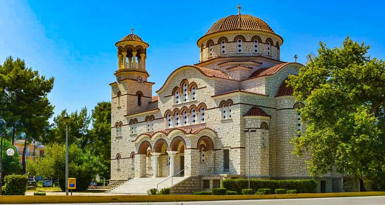 Stenen orthodoxe kerk met koepels en bogen onder een heldere blauwe hemel in Patras