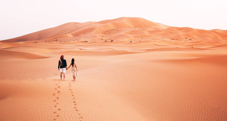 Couple marchant sur des dunes de sable rouge sous un ciel lumineux.