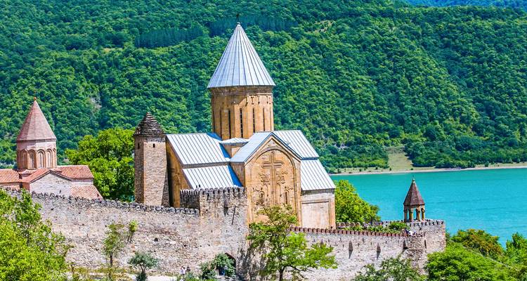 Complejo de fortaleza y iglesia de piedra Ananuri junto a un lago turquesa y colinas boscosas