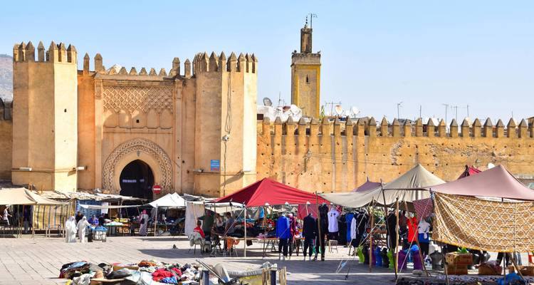 Una escena de mercado bullicioso con una muralla de fortaleza histórica en el fondo.