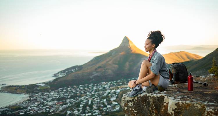 Femme profitant d'une vue sereine depuis un sommet de montagne avec un sac à dos à côté d'elle.