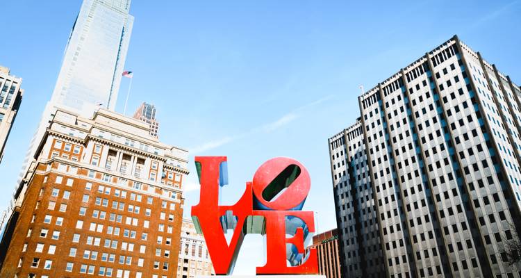 LIEFDE sculptuur in een stadspark met hoge gebouwen.