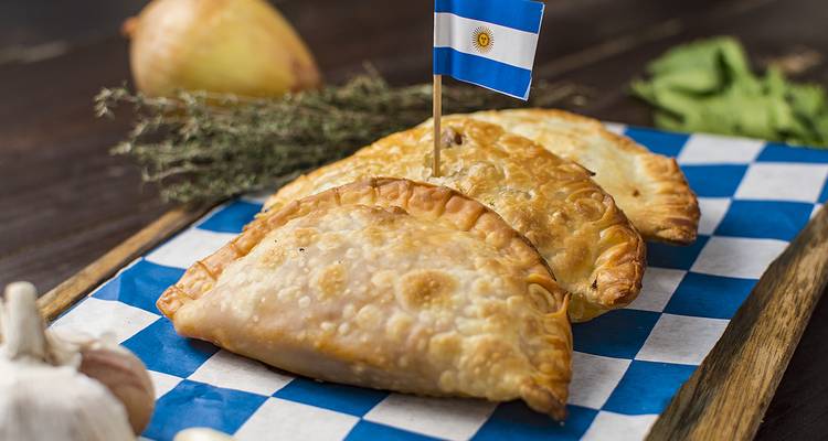 Empanadas on a checkered surface with an Argentine flag toothpick.