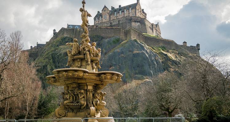 Fountain in a park with a historic castle on a rocky outcrop.