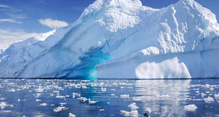 Gran iceberg con reflejos en agua tranquila bajo un cielo despejado.