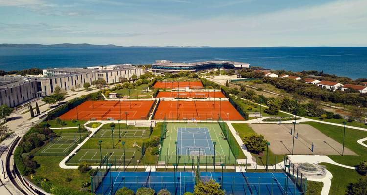 Luchtfoto van een tenniscomplex met verschillende banen nabij de zee.
