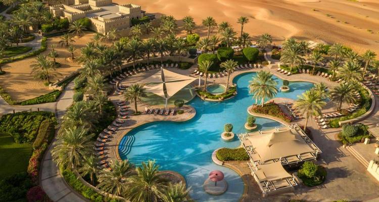 Luftaufnahme eines Luxusresorts mit Pools und Palmen in der Wüste.