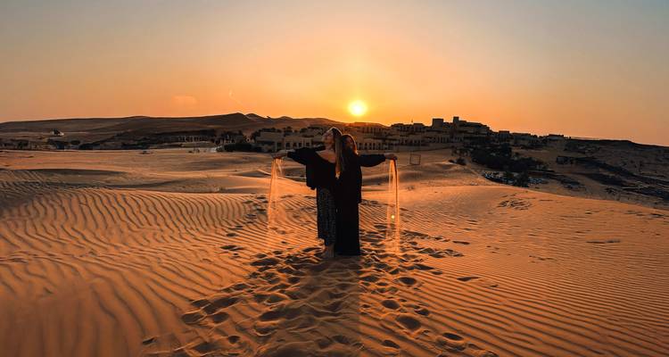 Person, die bei Sonnenuntergang in der Wüste steht, Sand rinnt durch ihre Hände.