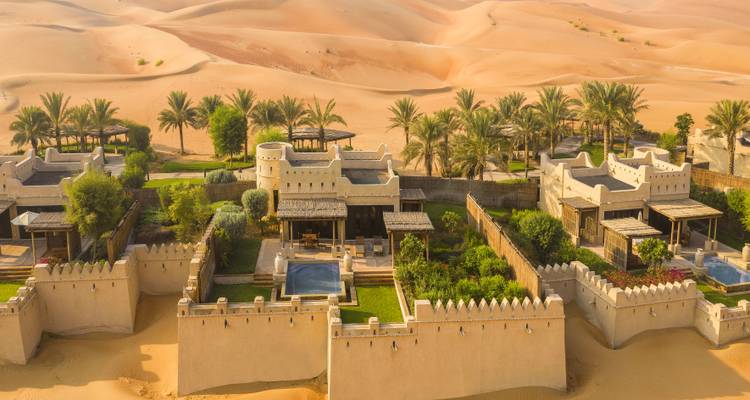 Luftaufnahme eines Wüstenresorts mit Palmen und Sanddünen.