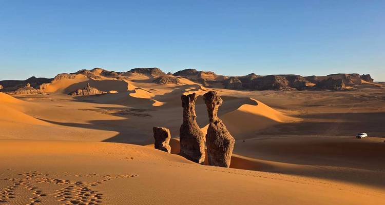 Des formations rocheuses uniques de grès s'élèvent depuis de vastes dunes dorées sous un ciel désertique limpide.