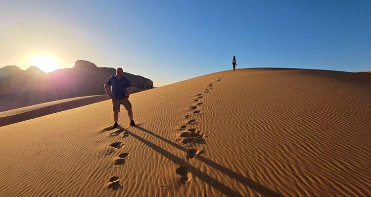 Deux voyageurs laissent des empreintes le long de la crête d'une dune de sable au lever du soleil, projetant de longues ombres.