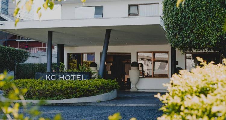 Entrada del Hotel KC con diseño arquitectónico moderno y plantas.