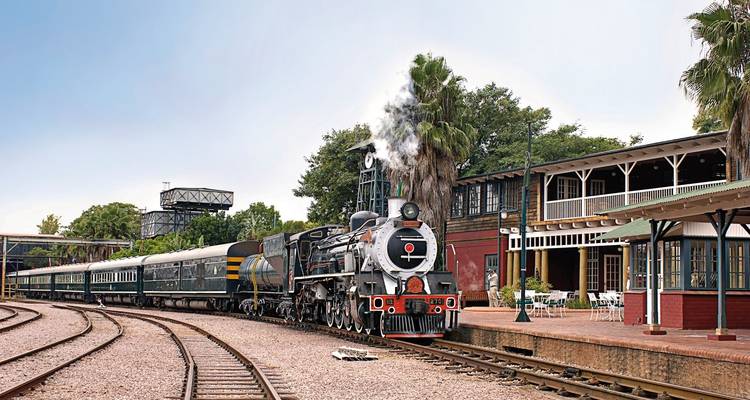 Historischer Dampfzug an einem Bahnhof mit Fahrgästen.