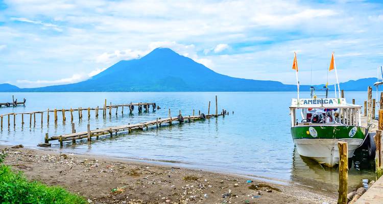 Bateau amarré à côté d'une jetée rustique sur le lac Atitlán avec un pic volcanique en arrière-plan sous un ciel bleu