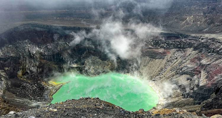 Lac de cratère turquoise fumant, entouré de parois rocheuses volcaniques escarpées