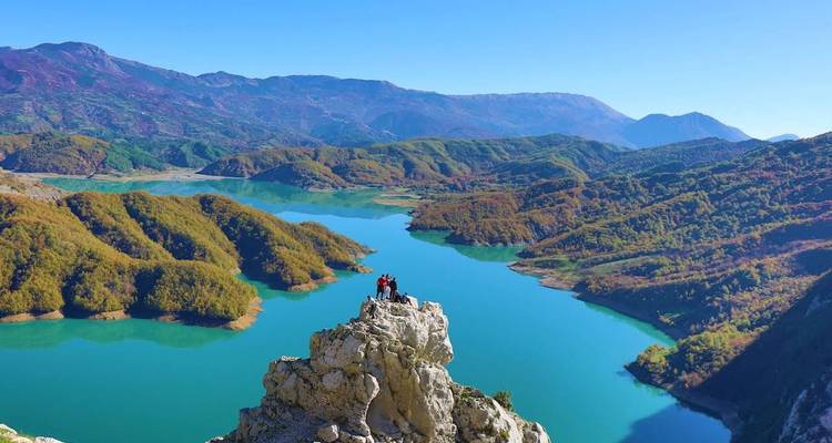 People standing on a rock overlooking a turquoise lake and mountains.