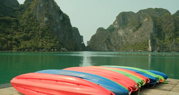 Des kayaks colorés alignés au bord de l'eau avec des collines calcaires en arrière-plan.