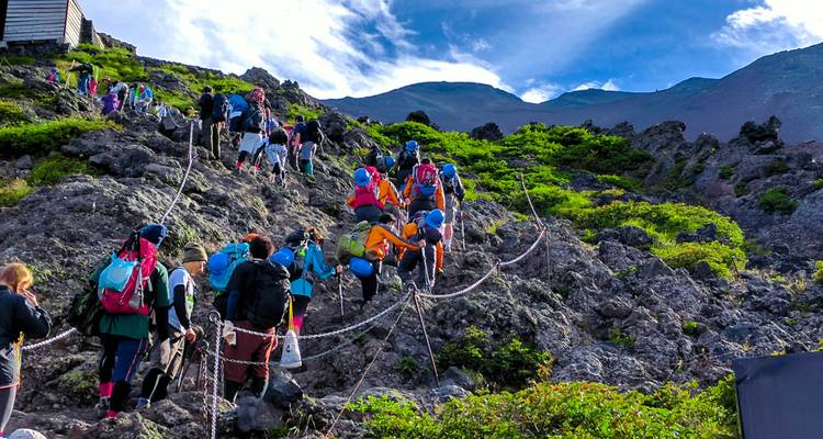 Hikers climbing a rocky path towards a mountain peak.