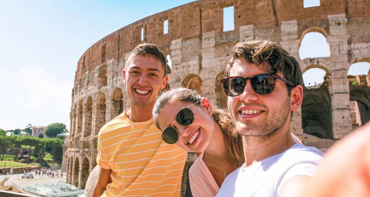 Three people taking a selfie in front of a large ancient amphitheater.
