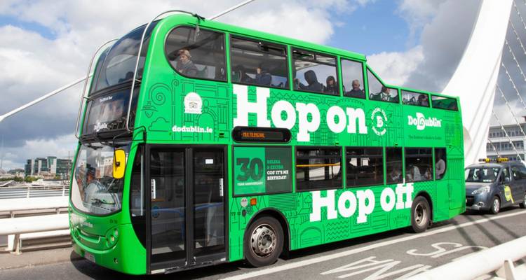Un autobús de dos pisos verde brillante de subir y bajar cruza un puente moderno de Dublín.
