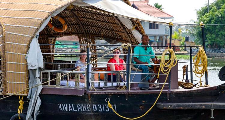 Los tradicionales cruceros en casa flotante de Kerala navegan por un exuberante canal de aguas tranquilas con turistas sentados.