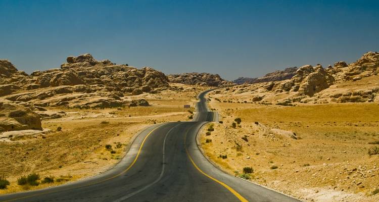 Carretera de asfalto larga y sinuosa que atraviesa un árido paisaje desértico rocoso bajo un cielo despejado.