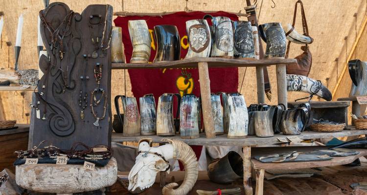 Étal de marché rustique présentant des cornes à boire sculptées, des bijoux et de l'artisanat de style viking à l'intérieur d'une tente.