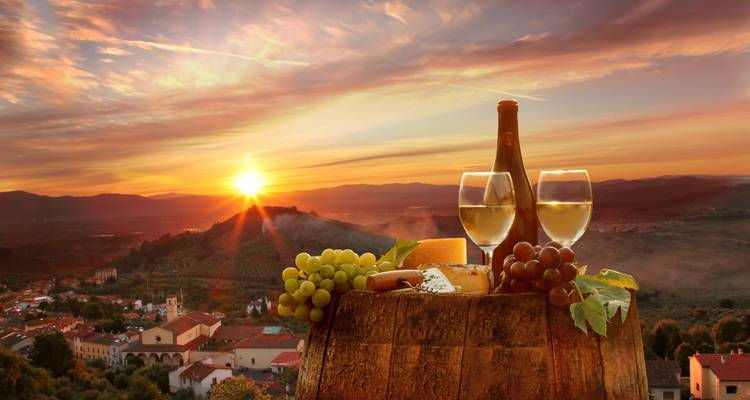 Grapes and wine with Tuscan landscape at sunset.