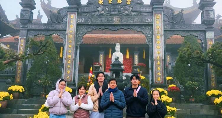 Travelers pose praying-style in front of a misty mountain pagoda complex with a white Buddha statue.