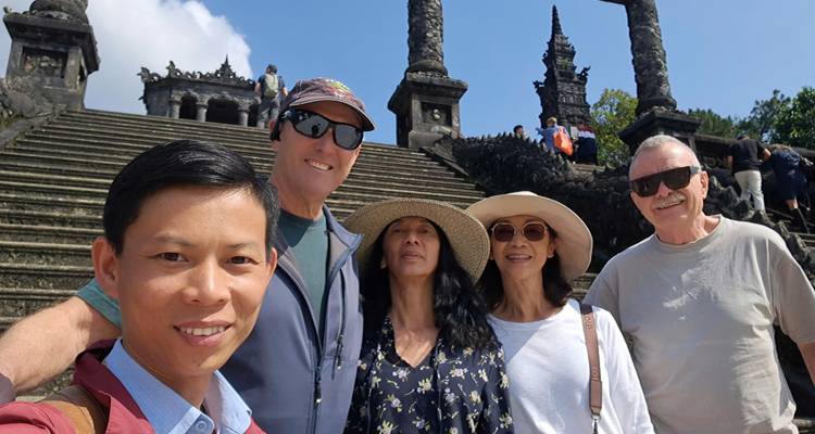 Selfie of five travelers on the staircase of Khai Dinh Tomb with ornate stone balustrades.