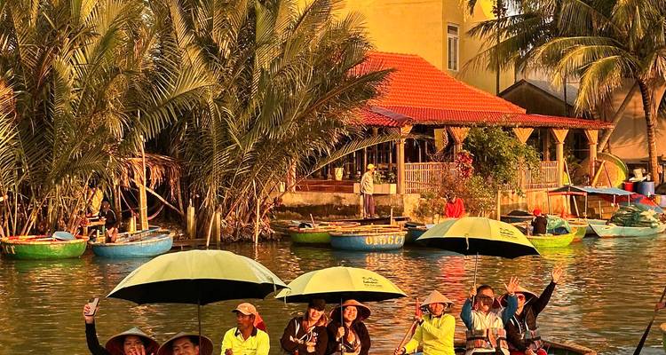 Series of basket boats with tourists holding umbrellas glide along a palm-lined river at golden hour.