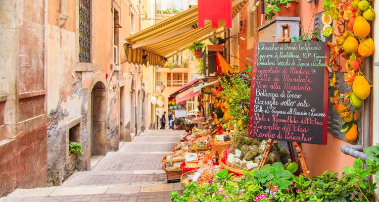 Calle europea estrecha con tiendas y flores.