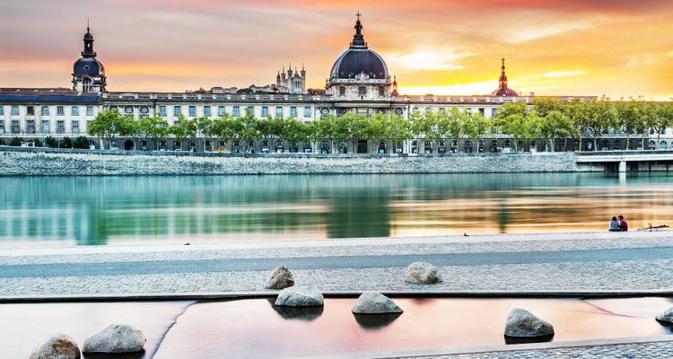 Sonnenuntergangsblick auf die Rhône-Uferpromenade in Lyon, Frankreich, mit historischer Architektur und Bäumen.