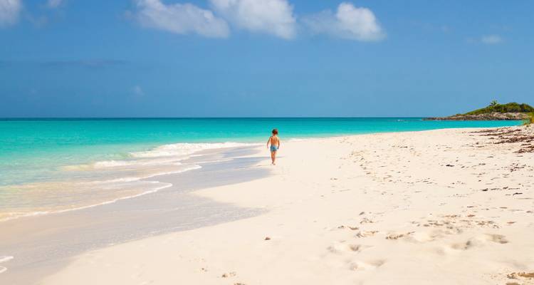 Persona caminando en una playa de arena blanca prístina con agua turquesa.